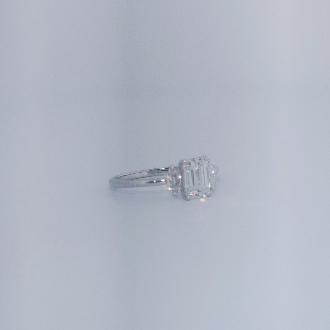 Female Wedding Ring, 14K White Gold, emerald-cut central Diamond (E/VS1, 1.02ct) flanked by 2 round Diamonds (0.25ct total).